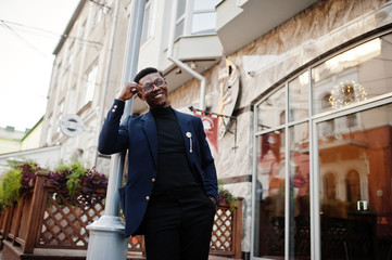 Amazingly looking african american man wear at blue blazer with brooch, black turtleneck and glasses posed at street. Fashionable black guy.