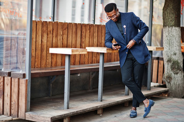 Amazingly looking african american man wear at blue blazer with brooch, black turtleneck and glasses posed at street. Fashionable black guy with mobile phone.