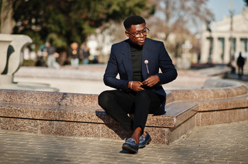 Obraz premium Amazingly looking african american man wear at blue blazer with brooch, black turtleneck and glasses posed at street. Fashionable black guy.