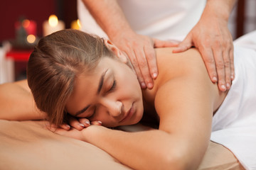 Fototapeta na wymiar Relaxed young woman enjoying soothing massage in the hands of skilled masseur. Spa therapist working with his female client, massaging her back at beauty center. Serenity, harmony, enjoyment concept