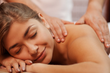 Obraz na płótnie Canvas Cropped close up of a beautiful happy healthy young woman smiling with her eyes closed, while professional masseur massaging her back and shoulder, copy space. Medical treatment, stress relief concept