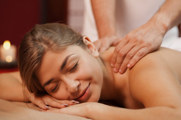 Fototapeta na wymiar Close up of a happy woman smiling while receiving back massage. Professional masseur working at his beauty clinic, massaging back of his client. Female enjoying spa treatment. Happiness, relax concept