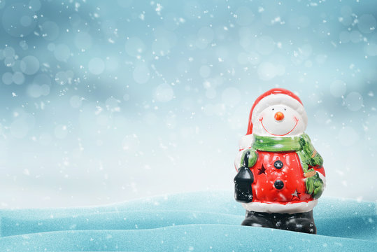 Cute snowman like Santa Claus on snow. Copy space on left side. Blue background with snowflakes and bokeh.