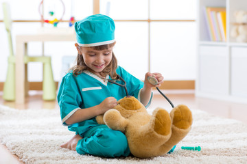 Smiling child girl playing with teddy bear and pretending she is a doctor in hospital