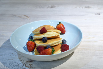 Japanese fluffy pancakes with berries on top on white wooden table.