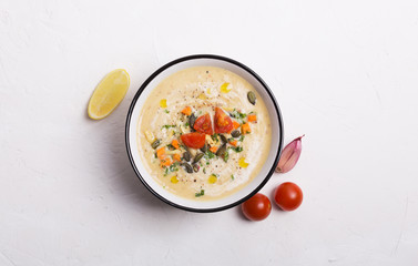 Lentil soup puree with tomatoes, cucumber and nuts in a bowl on a white wooden background