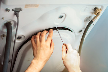 screwing the cover of the washing machine with a screwdriver after repair