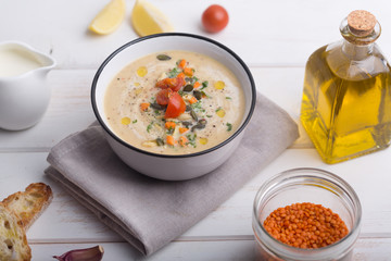 Lentil soup puree with tomatoes, cucumber and nuts in a bowl on a white wooden background