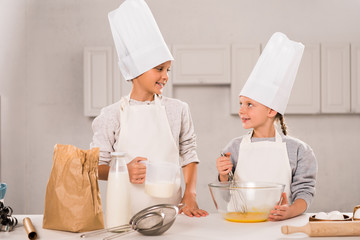 little boy with milk and sister looking at each other near table in kitchen