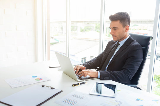 Handsome businessman working at desk with laptop and paper graph in office. Professional businessman and technology concept.