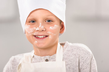 close up portrait of happy boy with flour on face in chef hat looking at camera