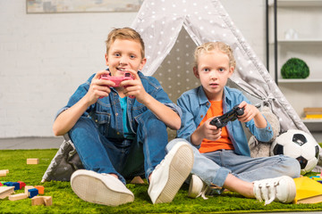 adorable sister and brother playing with joysticks near wigwam at home © LIGHTFIELD STUDIOS