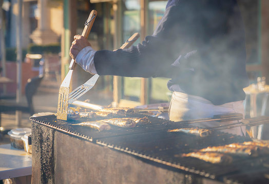 Fototapeta Man cooks herring on a grill on the market