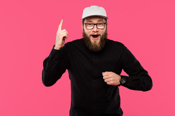 Naklejka premium excited bearded man in eyeglasses and cap hat doing idea gesture isolated on pink