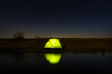 Night sky with stars over the tourist tent by the river. The landscape was photographed on a long exposure. © olgapkurguzova