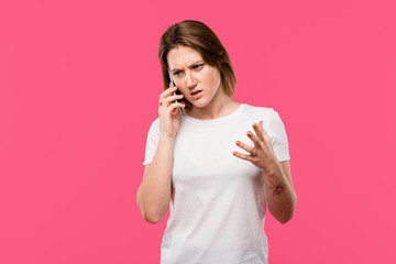aggressive girl with tattooed hand talking on smartphone and gesturing by hand isolated on pink