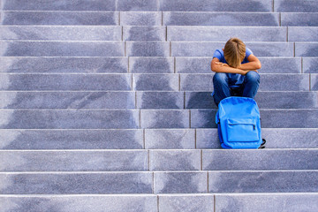 Upset boy covered his face with hands sitting on the stairs outdoors