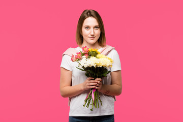 smiling young woman holding colorful bouquet from various flowers isolated on pink
