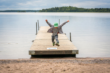 Front view of a young boy running  on a jetty and jumps in air towards a beach.