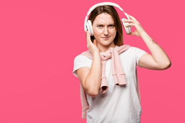 irritated young woman taking off headphones isolated on pink