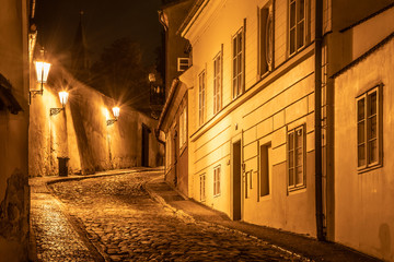 Fototapeta na wymiar Narrow cobbled street in old medieval town with illuminated houses by vintage street lamps, Novy svet, Prague, Czech Republic. Night shot.