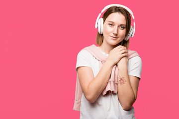 dreamy girl in headphones listening music and looking at camera isolated on pink