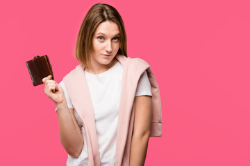 young woman holding wallet and looking at camera isolated on pink