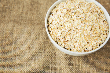 Oatmeal in white bowl on light brown textile background. Healthy eating