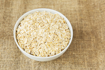 Oatmeal in white bowl on light brown textile background. Healthy eating