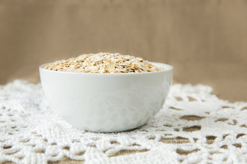 Oatmeal in white bowl on light brown textile background. Healthy eating