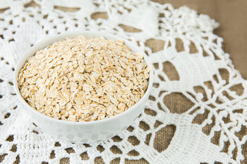 Fototapeta na wymiar Oatmeal in white bowl on light brown textile background. Healthy eating