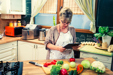 Mature  woman using digital tablet while cooking in the kitchen.