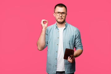 young man holding empty wallet and showing zero sign isolated on pink