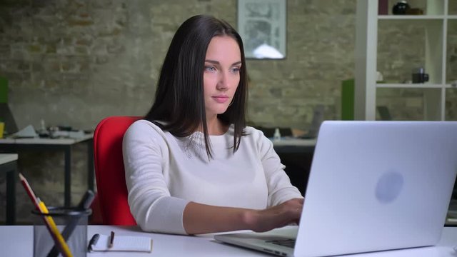 Woman working in the office in front of the laptop and typing interestedly