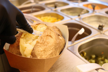 Chef cook in black gloves is making Kumpir - Turkish traditional meal with baked potato, butter, cheese, and vegetables in Restaurant.
