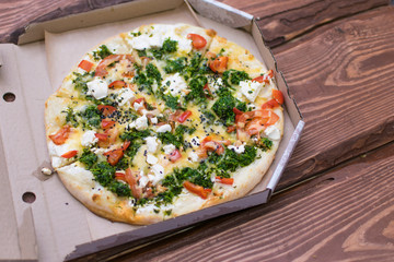 Pizza with feta and spinach in a cardboard box on a dark wooden background.