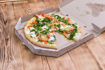 Pizza with feta and spinach in a cardboard box on a light wooden background.