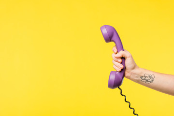 cropped shot of person holding purple handset isolated on yellow