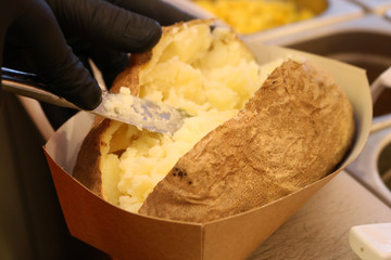 Chef cook in black gloves is making Kumpir - Turkish traditional meal with baked potato, butter, cheese, and vegetables in Restaurant.