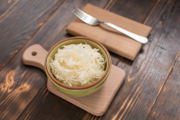 Sauerkraut in a plate on a wooden background.