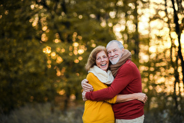 A senior couple standing in an autumn nature at sunset, hugging. Copy space.
