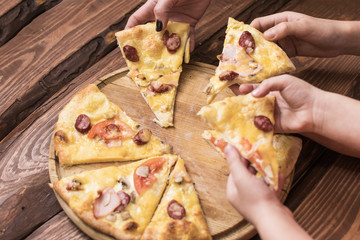 Hands take pieces of pizza on a dark wooden background.