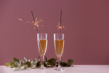 Festive Christmas sparklers in glasses with champagne on table against color background
