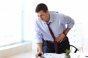 Young businessman suffering from abdominal pain in office
