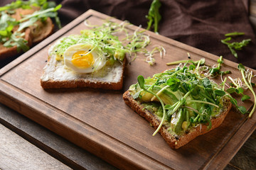 Tasty toasts with avocado and fried egg on wooden board