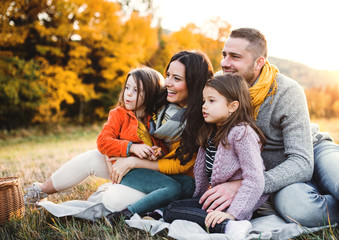 Fototapeta premium A portrait of young family with two small children in autumn nature at sunset.
