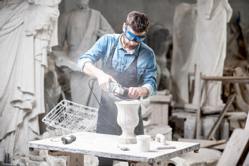 Sculptor in workware grinding stone vase at the working space in the old atmospheric studio - obrazy, fototapety, plakaty