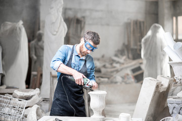 Sculptor in workware grinding stone vase at the working space in the old atmospheric studio