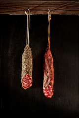 Two pieces of Fuet hanging in front of a rustic wall. Traditional sausage of Catalonia, Spain.