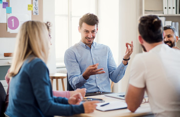 Group of young businesspeople sitting around table in a modern office, having meeting.